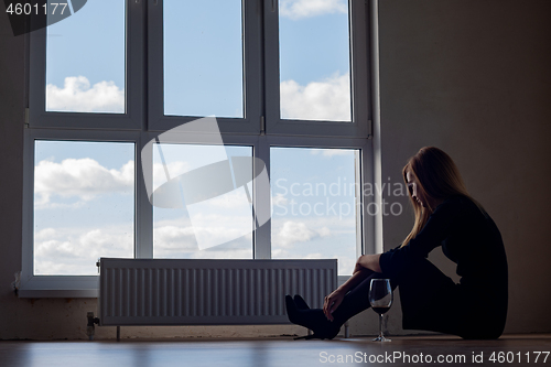 Image of A girl with a glass of wine sits on the floor at a large stained glass window