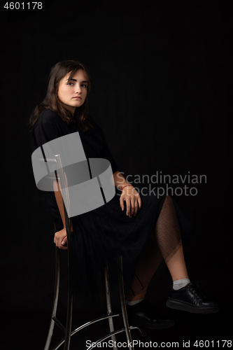 Image of Fifteen-year-old girl sits on a bar chair, snasked on a black background in a dark