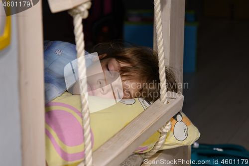 Image of The girl fell asleep on the edge of the bed, next to the rope ladder on the second tier