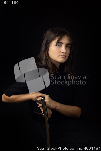 Image of Portrait of a fifteen-year-old girl on a black background, a girl clouded on the back of a chair