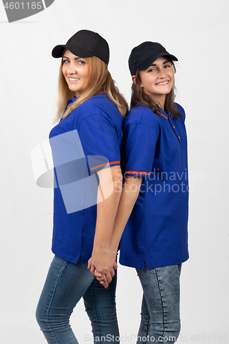 Image of Two different-aged girls of European appearance in the same clothes stand with their backs to each other