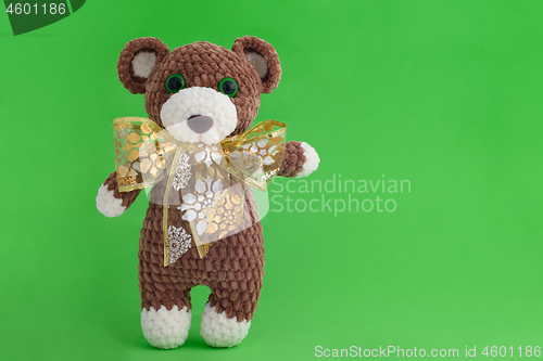 Image of Children\'s knitted toy bear with bow on a green background