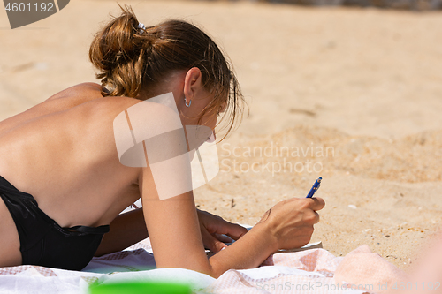 Image of Girl on the beach is engaged in self-learning, solves problems in a notebook