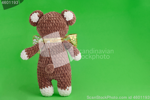 Image of Children\'s knitted toy bear with bow on a green background