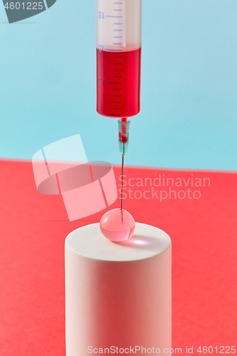 Image of Injection of syringe with red liquid into small ball on cylinder.