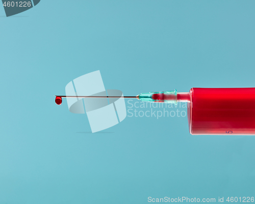 Image of Close-up needle of plastic syringe with drop of red liquid.