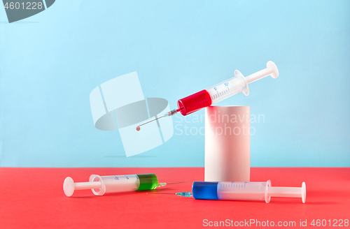 Image of Two syringes with vaccine and one with red drop on a plaster cylinder.