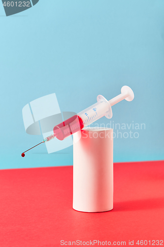 Image of Disposable syringe with drop of red liquid on a plaster cylinder.