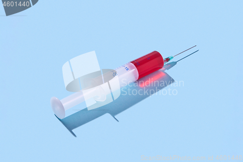 Image of Disposable syringe of red vaccine with hard shadow.