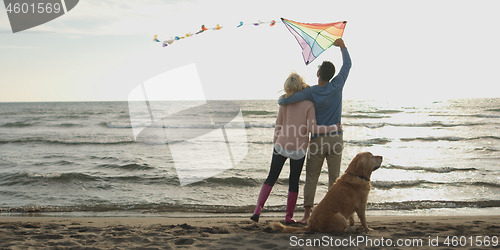 Image of couple with dog having fun on beach on autmun day