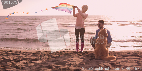 Image of couple with dog having fun on beach on autmun day