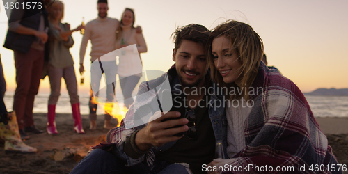 Image of Couple enjoying bonfire with friends on beach