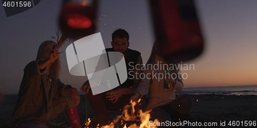 Image of Young Friends Making A Toast With Beer Around Campfire at beach