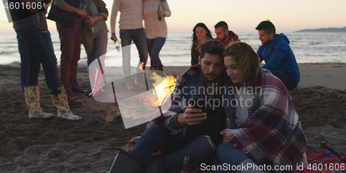 Image of Couple enjoying bonfire with friends on beach