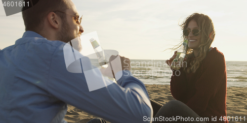 Image of Loving Young Couple Sitting On The Beach beside Campfire drinkin