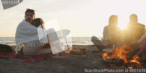 Image of Loving Young Couple Sitting On The Beach beside Campfire drinkin