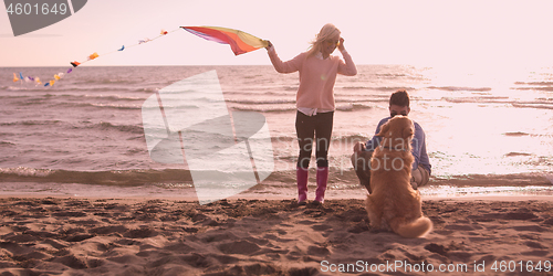 Image of couple with dog having fun on beach on autmun day