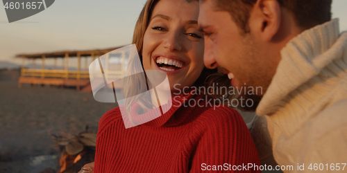 Image of Loving Young Couple Sitting On The Beach beside Campfire drinkin