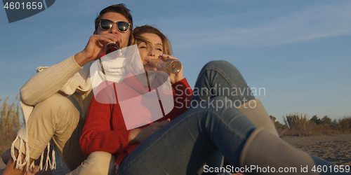 Image of Loving Young Couple Sitting On The Beach beside Campfire drinkin