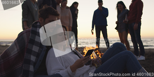 Image of Couple enjoying bonfire with friends on beach