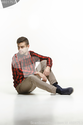 Image of Casual young man sitting on the floor and looking to a side, away from the camera, on a white background