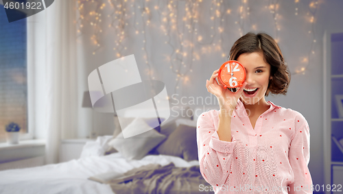 Image of happy young woman in pajama with alarm clock