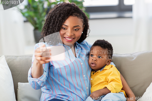 Image of african mother with baby son taking selfie at home