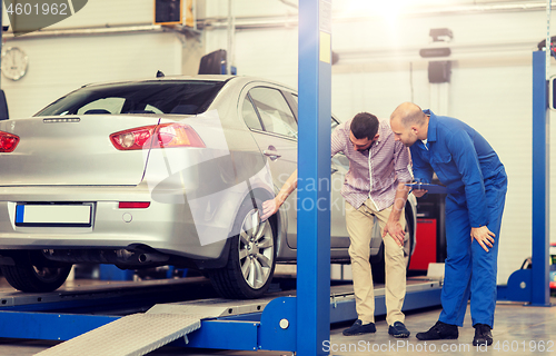 Image of auto mechanic with clipboard and man at car shop