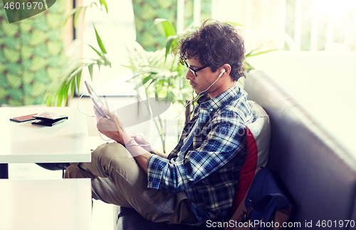 Image of man with tablet pc and earphones sitting at cafe