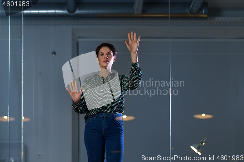 Image of businesswoman using glass wall at night office