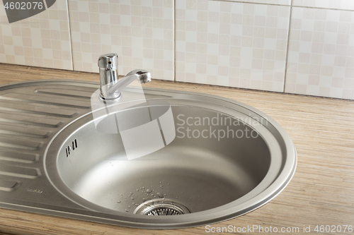 Image of Clean round metal kitchen sink with faucet and water drops from leak