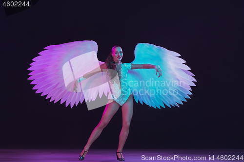 Image of Young female dancer with angel\'s wings in neon light on black background