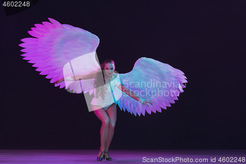 Image of Young female dancer with angel\'s wings in neon light on black background