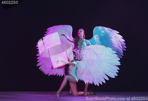 Image of Young female dancers with angel\'s wings in neon light on black background