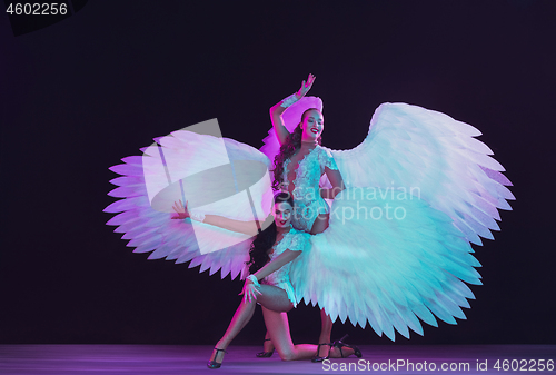 Image of Young female dancers with angel\'s wings in neon light on black background