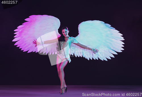 Image of Young female dancer with angel\'s wings in neon light on black background