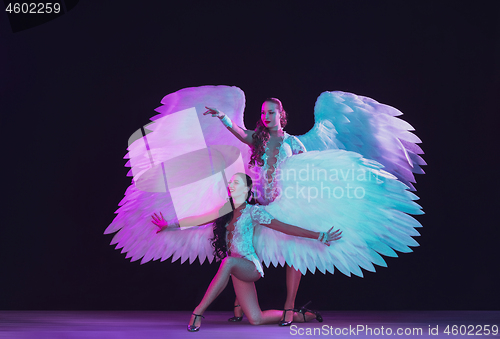 Image of Young female dancers with angel\'s wings in neon light on black background