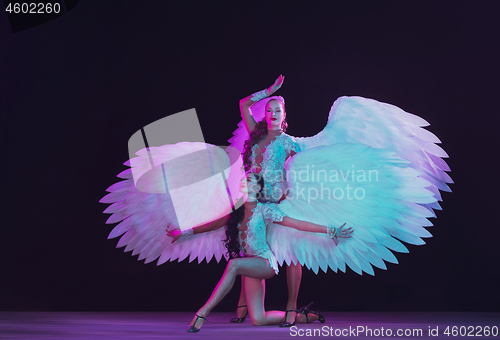 Image of Young female dancers with angel\'s wings in neon light on black background