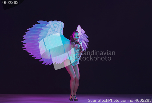 Image of Young female dancer with angel\'s wings in neon light on black background