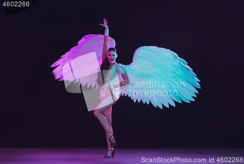 Image of Young female dancer with angel\'s wings in neon light on black background