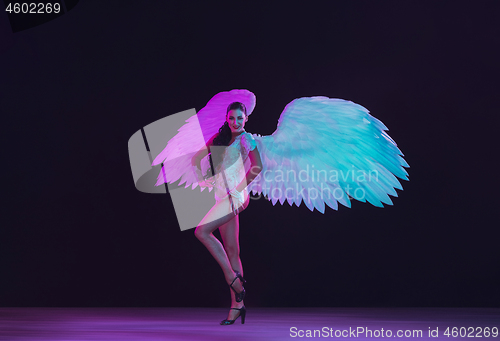 Image of Young female dancer with angel\'s wings in neon light on black background