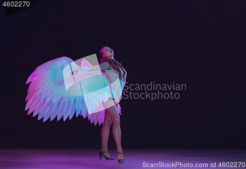 Image of Young female dancer with angel\'s wings in neon light on black background