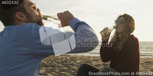 Image of Loving Young Couple Sitting On The Beach beside Campfire drinkin