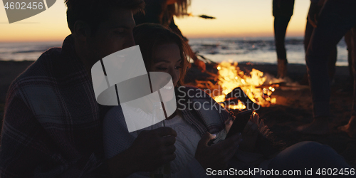 Image of Couple enjoying bonfire with friends on beach