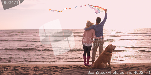 Image of couple with dog having fun on beach on autmun day