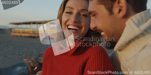 Image of Loving Young Couple Sitting On The Beach beside Campfire drinkin