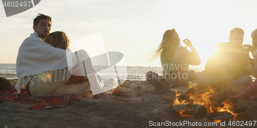 Image of Loving Young Couple Sitting On The Beach beside Campfire drinkin