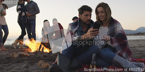 Image of Couple enjoying bonfire with friends on beach