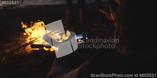 Image of Couple taking photos beside campfire on beach