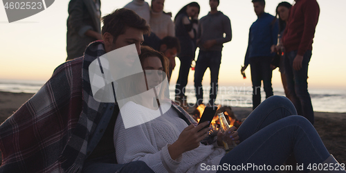 Image of Couple enjoying bonfire with friends on beach